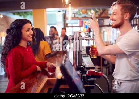 Barman souriant derrière le comptoir servant une cliente féminine avec de la bière Banque D'Images