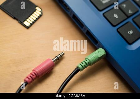 Câbles d'écouteurs connectés à un ordinateur portable bleu moderne, une mémoire USB et une mémoire SD sur une table en bois Banque D'Images