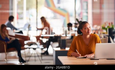 Jeune femme d'affaires assise au bureau écrivant dans un ordinateur portable dans un bureau ouvert moderne Banque D'Images