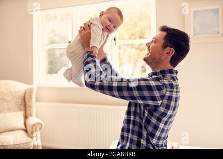 Le Père aimant lever bébé fils dans l'air comme ils jouent à la maison ensemble Banque D'Images