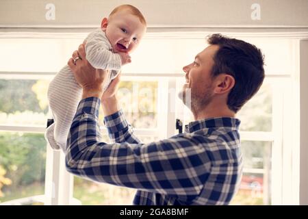 Le Père aimant lever bébé fils dans l'air comme ils jouent à la maison ensemble Banque D'Images