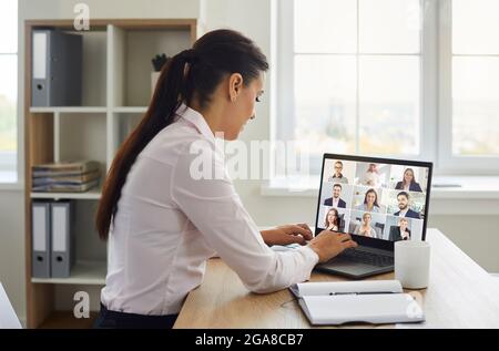 Femme assise au bureau avec ordinateur portable et ayant des réunions avec une équipe de collègues Banque D'Images