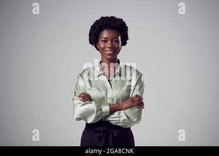 Studio Portrait de jeune femme d'affaires souriante avec bras pliés sur fond Uni Banque D'Images