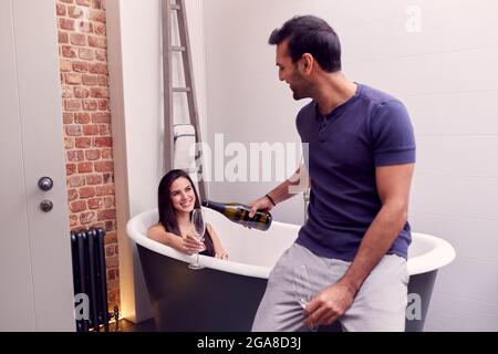 Couple avec un homme servant du champagne à une femme couché à Bath à la maison Banque D'Images