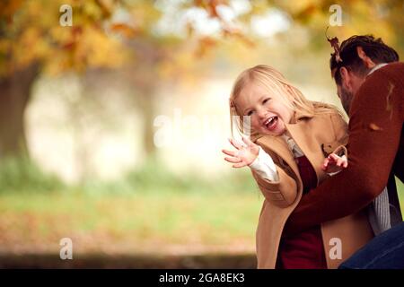 Jeune fille jetant des feuilles d'automne dans l'air comme elle a amusant de jouer dans le jardin avec le Père Banque D'Images