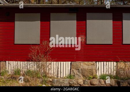 Les fenêtres d'une maison rouge sont arraisonnées avec des plaques de métal. Banque D'Images