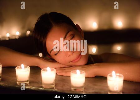Belle femme dans le jacuzzi avec bougies allumées au spa Banque D'Images