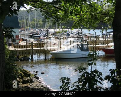 Encadré par des arbres, une photo des yachts et des bateaux à moteur amarrés aux jetées de la marina, Bowness sur le lac Windermere, le quartier des lacs anglais. Banque D'Images