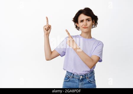 Elle n'aime pas ça. Sceptique brunette jeune fille étudiant frowning, pointant vers le coin supérieur gauche et se terrer douteux, incrédulité, méchante smth, négatif Banque D'Images