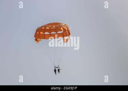 Parachute ascensionnel orange haut dans le ciel avec deux personnes sur le parachute ascensionnel Banque D'Images