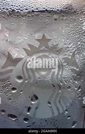 Des gouttes de condensation s'accrochent sur le côté d'une tasse à boisson jetable en plastique transparent remplie d'eau glacée montrant le logo de la chaîne à café Starbucks Banque D'Images