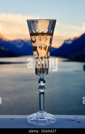 Vue rapprochée d'une flûte en cristal remplie de vin rose en face d'une vue pittoresque sur le lac de montagne au coucher du soleil. Banque D'Images