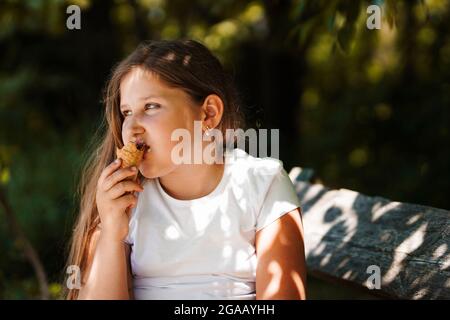 Caucasienne fille assise sur le banc et manger de la crème glacée . Un enfant souriant et rêvant. Heure d'été. Banque D'Images