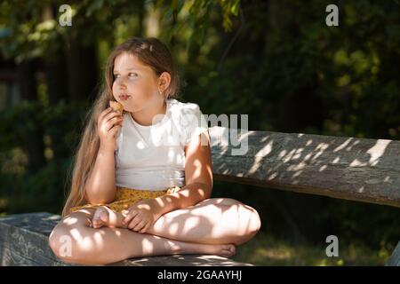 Caucasienne fille assise sur le banc et manger de la crème glacée . Un enfant souriant et rêvant. Heure d'été. Bonne enfance. Banque D'Images