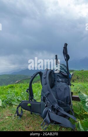 Un sac à dos touristique avec des bâtons de randonnée se dresse parmi l'herbe dans les montagnes. Sur fond de nuages de pluie Banque D'Images