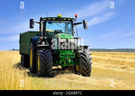 Tracteur agricole John Deere 6155R et remorque agricole Kire pleine de blé récolté au champ par une belle journée. Salo, Finlande. 25 juillet 2021. Banque D'Images