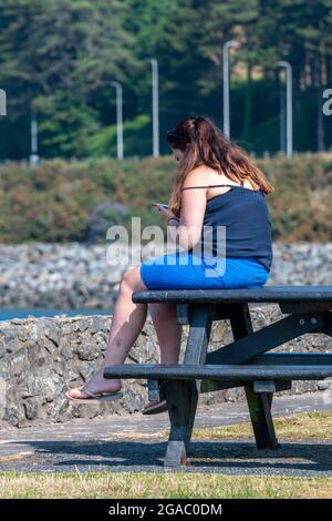 jeune femme regardant un téléphone, femme assise sur une table regardant un smartphone, adolescente regardant un appareil mobile, jeune femme utilisant un smartphone, été Banque D'Images