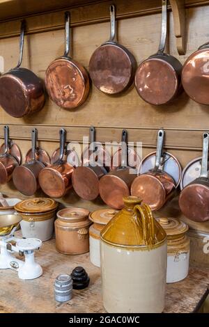 casseroles et pots à fond de cuivre accrochés au mur d'une cuisine historique avec des pots en pierre et des drapeaux au premier plan. Banque D'Images