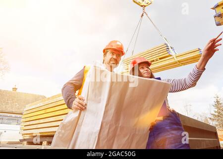 Livraison de bois et de matériaux de construction au chantier de construction avec deux ouvriers de construction et un plan de construction Banque D'Images