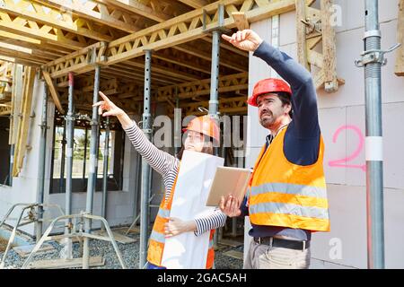 Les artisans et les architectes ayant un plan de construction discutent de l'organisation et de la planification de la construction avant la construction de la coquille Banque D'Images