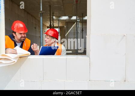 Architecte avec liste de contrôle et contremaître discutant du projet de construction dans la coquille du chantier de construction Banque D'Images