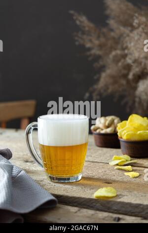 Verre avec bière et mousse et chips avec noix sur fond de bois, vacances d'automne avec une bière rafraîchissante Banque D'Images