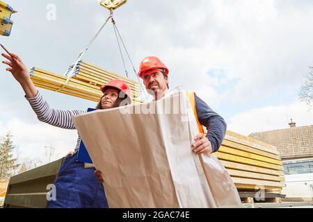 Architecte et artisan avec plan sur le chantier de construction avec matériaux de construction sur la grue en arrière-plan Banque D'Images