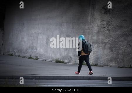 Un homme à capuchon avec sac à dos marche près d'un mur dans une rue. Banque D'Images