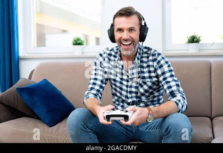 Homme jouant à des jeux d'ordinateur, jouant à la console, tenant des coussins dans les mains Banque D'Images