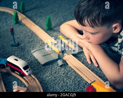 Garçon regarde le train de course à pied. Chemin de fer en bois et visage d'enfant. Concept de l'enfance, jeux pour enfants Banque D'Images