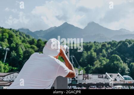 L'homme de la tour d'observation des jumelles à bouton-actionné regarde les montagnes. Vue de l'arrière. Banque D'Images