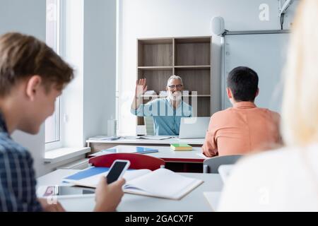 Un professeur gai agité se fait la main aux élèves sur un premier plan flou dans la salle de classe Banque D'Images