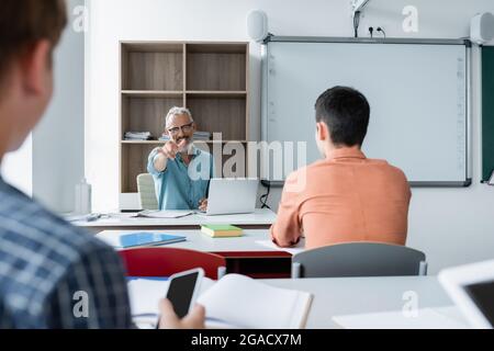 Professeur souriant pointant du doigt près des écoliers et des gadgets dans la salle de classe Banque D'Images