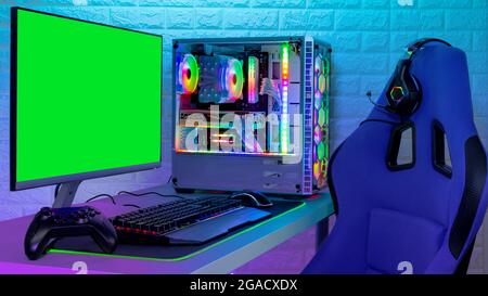 PC de jeu RVB lumineux et coloré avec clavier, souris, moniteur et chaise avec course à l'écran devant un mur en pierre de brique lumineuse LED. Ordinateur Banque D'Images