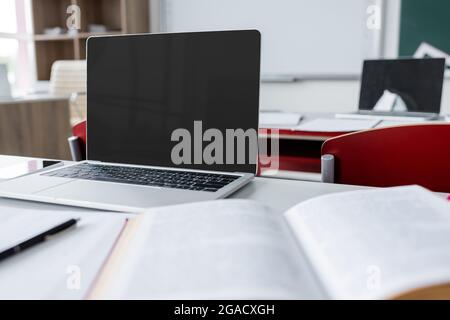 ordinateur portable moderne avec écran vierge près d'un manuel flou sur le bureau de l'école Banque D'Images