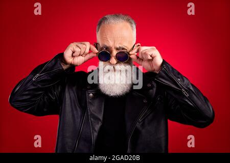 Photo de l'homme beau et vieux sérieux confiant main toucher lunettes de soleil hipster cool isolé sur fond de couleur rouge Banque D'Images