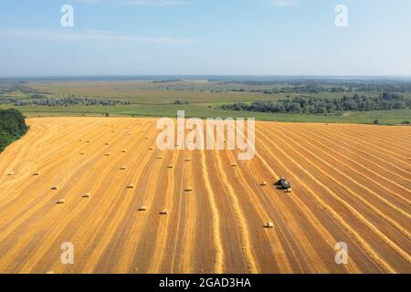 Beaucoup de balles de paille dans un champ faubouré : le tracteur emballe de la paille en balles, tir de drone aérien. Récolte de la paille dans le champ en été : le tracteur collecte la paille et l'emballe en balles Banque D'Images