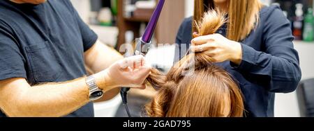 Deux coiffures utilisant le fer à friser sur les clients cheveux longs bruns dans un salon de beauté Banque D'Images