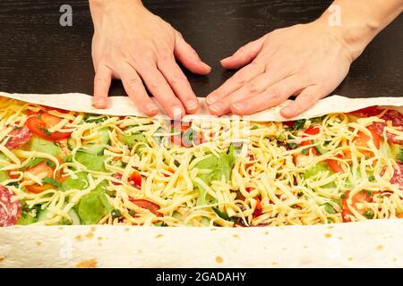 les mains des femmes enveloppent la salade de légumes frais avec du fromage dans du pain pita. la cuisson du shawarma sur une table en bois noir Banque D'Images