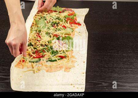 les mains des femmes enveloppent la salade de légumes frais avec du fromage dans du pain pita. la cuisson du shawarma sur une table en bois noir Banque D'Images