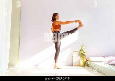 Femme sportive d'âge moyen attirante brunette pratiquant le yoga, faisant des exercices d'étirement tout en se tenant debout dans la posture étendue de la main à gros orteil, utthita ha Banque D'Images