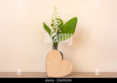 Petit bouquet de lys de la vallée en bouteille et coeur en bois vierge avec espace pour le design sur fond beige Banque D'Images