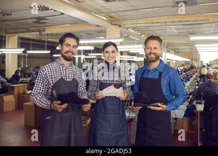 Portrait des travailleurs heureux de l'usine de chaussures montrant de nouvelles chaussures et souriant à l'appareil photo Banque D'Images