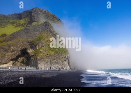 plage noire de reynisfjoru un jour ensoleillé avec ciel bleu un brouillard de mer cloque le bord de reynisfjall dans une scène atmosphérique Banque D'Images