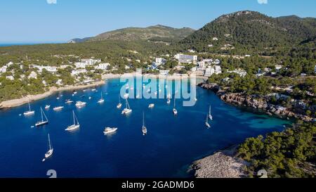 Vue aérienne de la baie de Portinatx sur la rive nord de l'île d'Ibiza en Espagne - bateaux ancrés près d'une plage de sable entourée de forêts de pins Banque D'Images