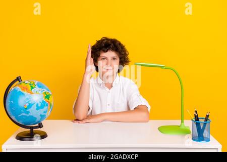 Photo de mignon drôle école garçon porter chemise blanche sourire bureau de séance lever bras isolé couleur jaune fond. Banque D'Images