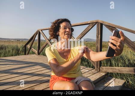 Une femme joyeuse et vitale, dans les années 70, prend un selfie avec son téléphone mobile, dans le parc naturel du Prat de Cabanes, en Méditerranée, en Espagne Banque D'Images