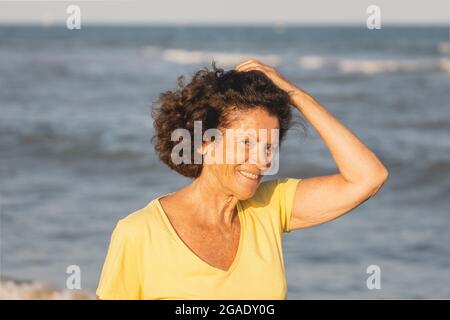Une femme joyeuse et vitale, dans ses années 70, marche sur une plage au coucher du soleil, sur les rives de la Méditerranée, en Espagne Banque D'Images