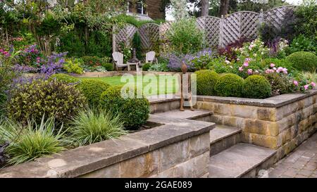 Jardin privé paysagé coloré en été (design contemporain, terrasses et terrasse, sièges de patio, pelouse, sculpture) - Yorkshire, Angleterre, Royaume-Uni. Banque D'Images