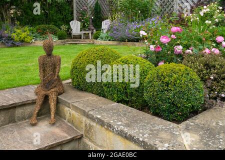 Sculpture (élément ornemental) dans un magnifique jardin paysagé coloré (plantes à fleurs, arbustes, boules, pelouse, chaises) - Yorkshire Angleterre Royaume-Uni Banque D'Images